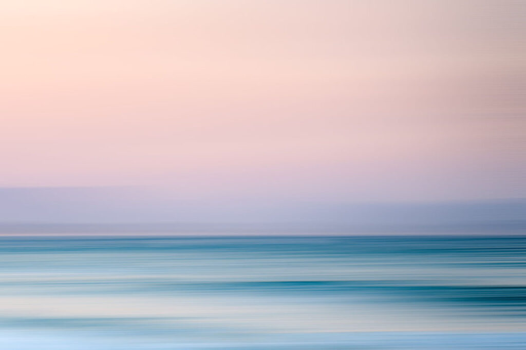 Calm ocean and pink sky, slightly blurry from horizontal motion with slow shutter.